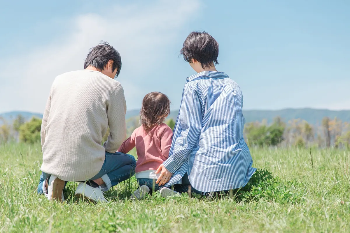 草原にしゃがむ家族の後ろ姿