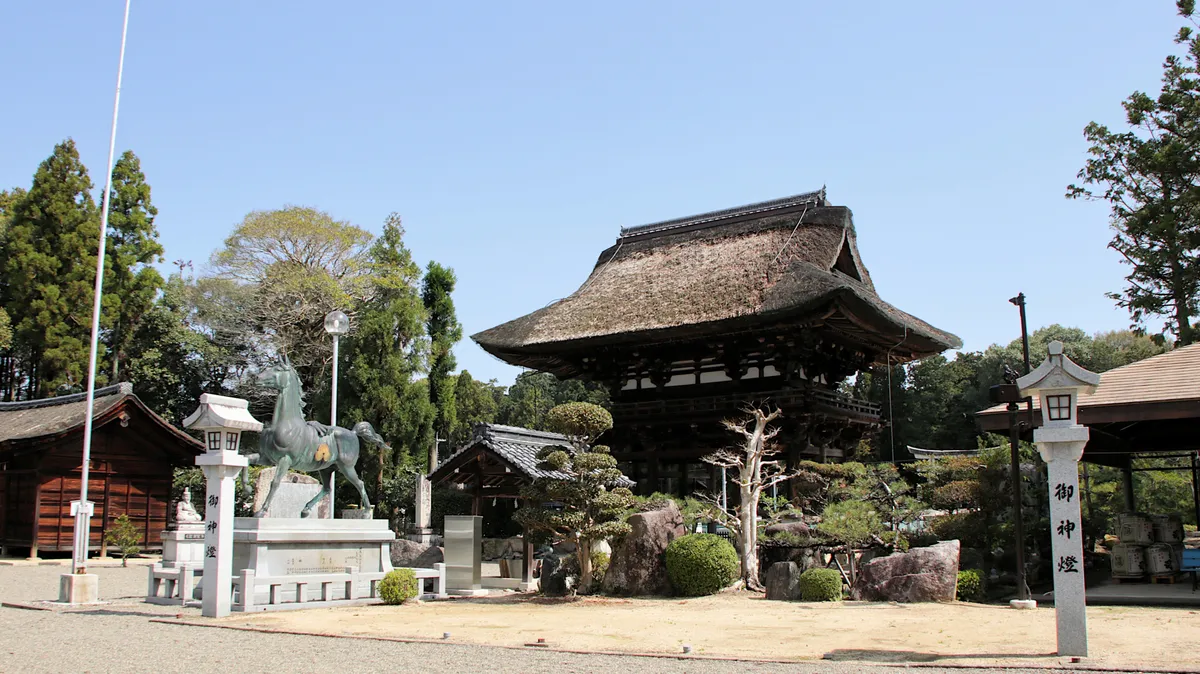 茅葺き屋根の神社と神馬像